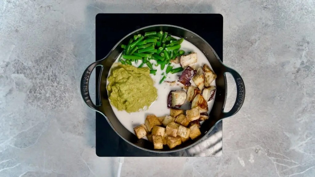 A variety of vegetables and tofu in a pot with coconut milk and green curry paste for vegan green curry