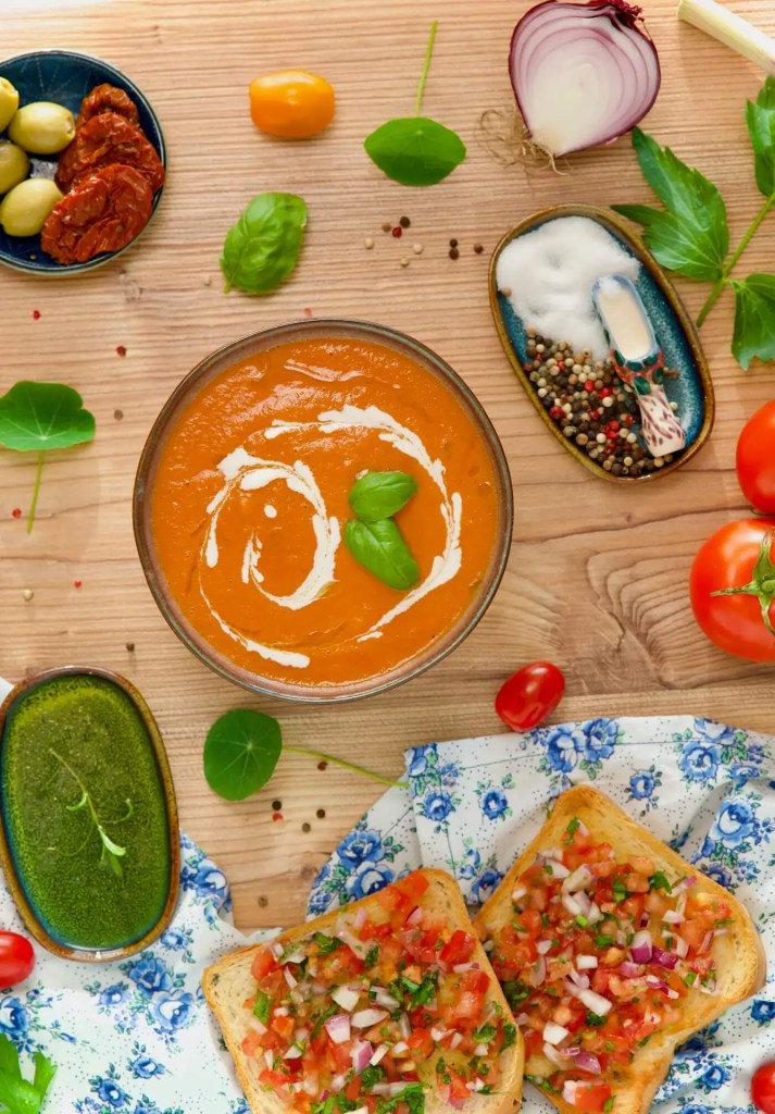 Tomatensuppe, umgeben von Tomaten, Basilikum und anderen Gewürzen